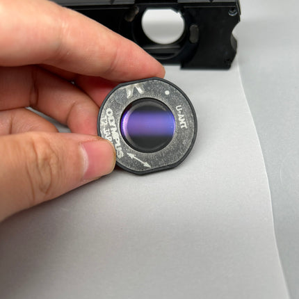 Person holding Olympus BX DIC Kit U-UCDB-2 Universal Condenser lens with purple tint for microscopy.