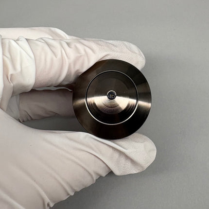 Close-up of a hand holding a circular metal component, showcasing its polished surface and central feature.